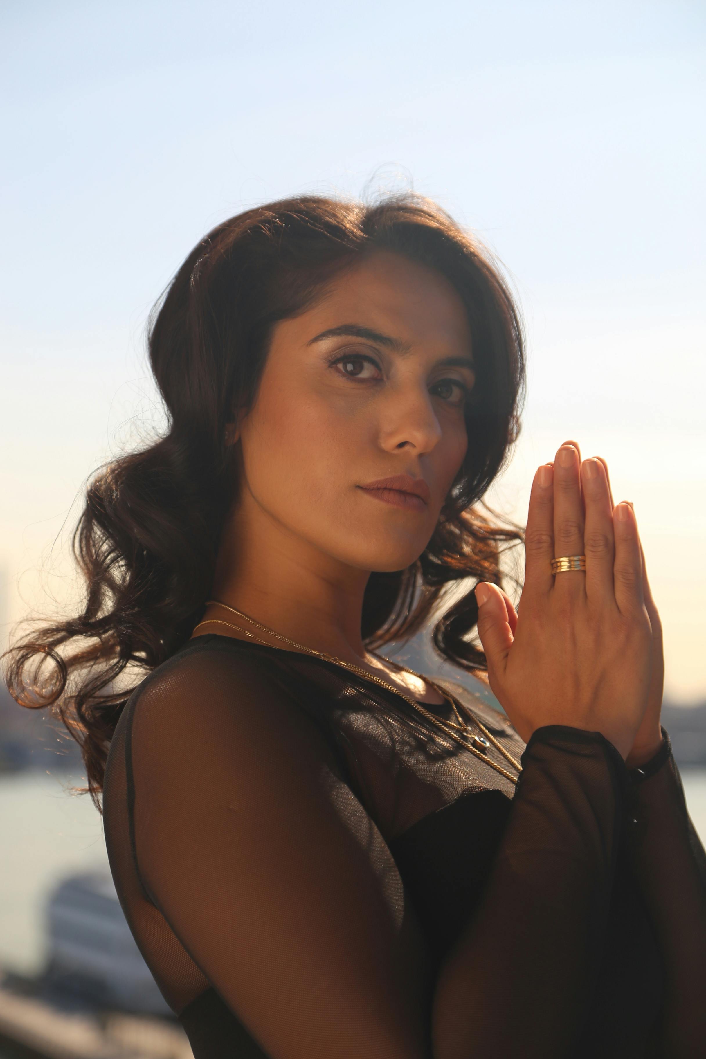 A serene portrait of a woman with hands together, set against a Hoboken background.