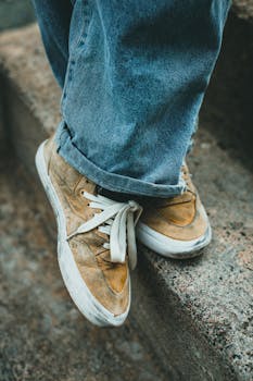 Stylish denim and sneakers fashion on outdoor stairs, focusing on worn out footwear.