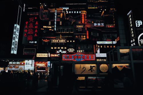 Free A bustling city street illuminated by vibrant neon signs and bustling activity during the night. Stock Photo