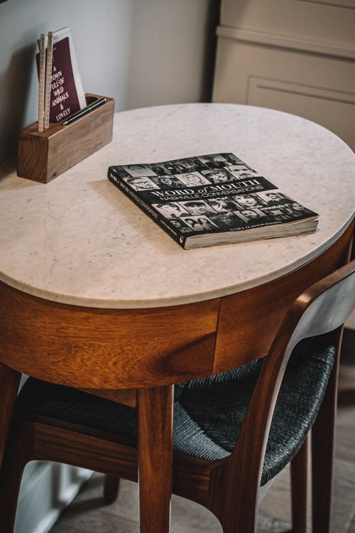 Free Cozy interior with a marble top table, book, and magazine rack, offering a warm reading space. Stock Photo