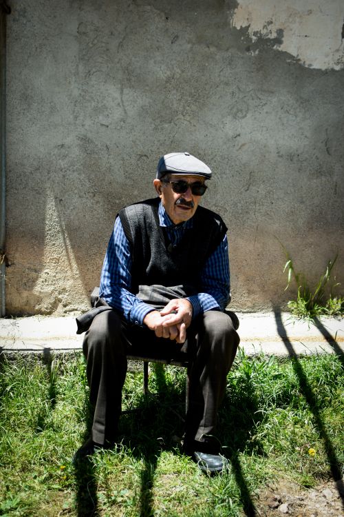Free Elderly man in sunglasses and cap sitting outside on a sunny day, relaxing. Stock Photo