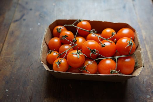 A wooden table with a cardboard box filled with vibrant cherry tomatoes, highlighting freshness.