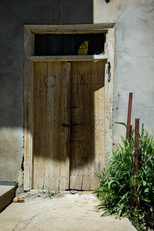 Free Old wooden door with cracks and shadows in daylight, surrounded by grass. Stock Photo