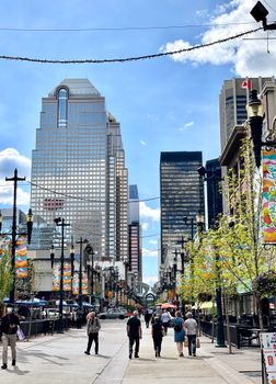 A bustling scene captures people walking down an energetic street flanked by tall skyscrapers in Calgary.