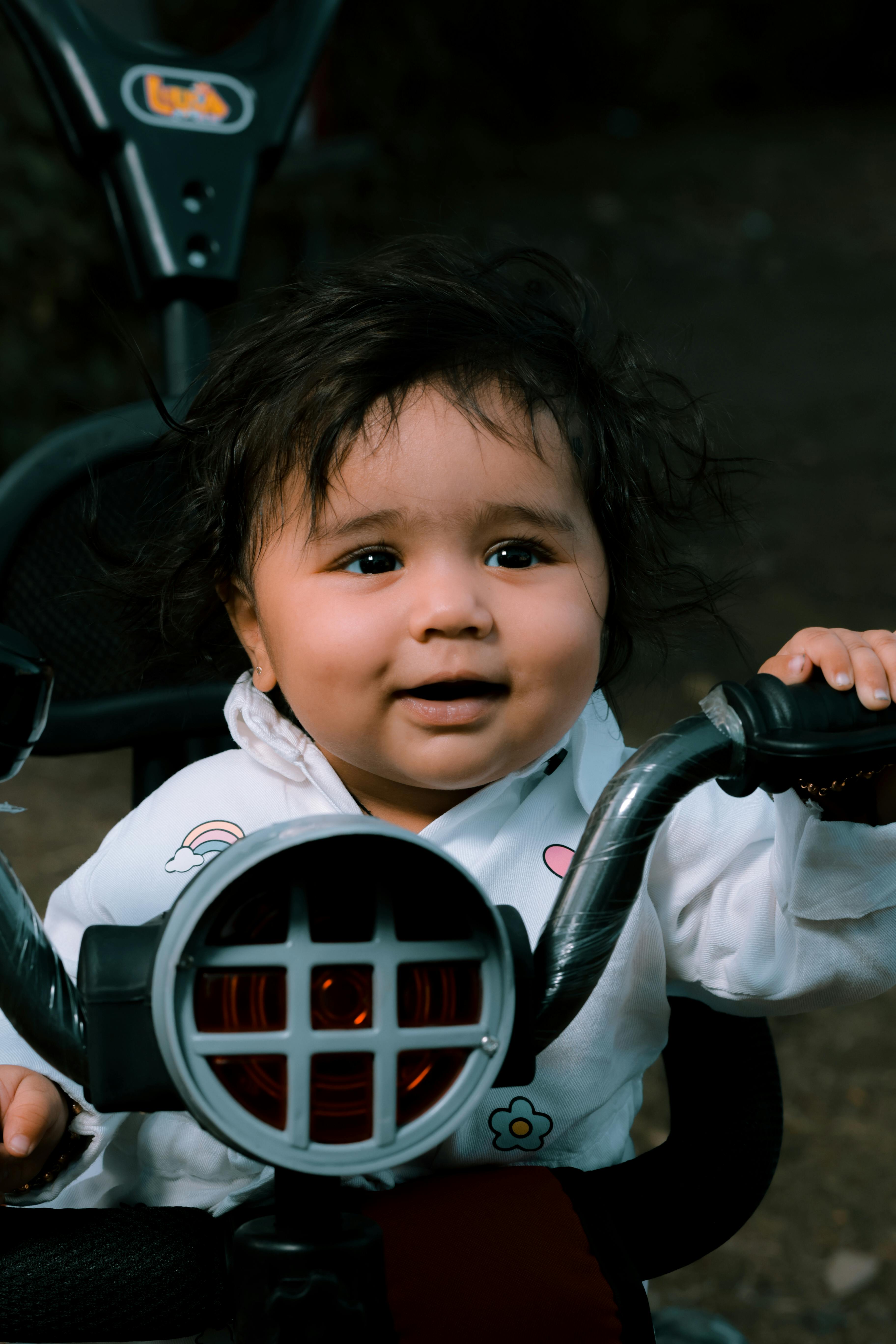 Charming child sitting on a tricycle with a joyful expression, outdoors.
