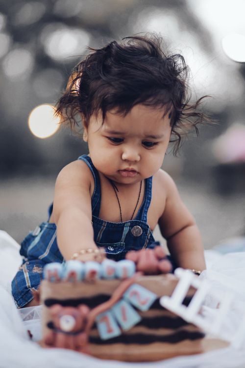 Free Cute baby in denim jumper playing outdoors with a blurred background. Captures innocence and exploration. Stock Photo