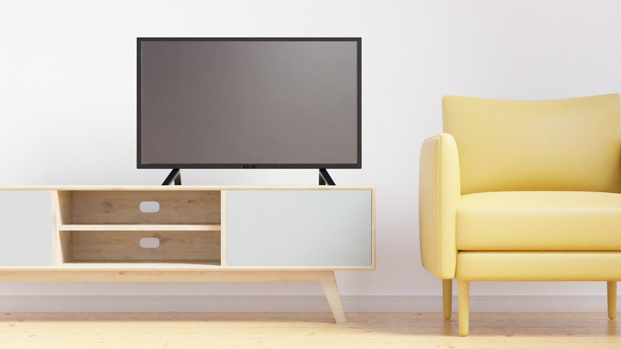Flat-screen TV on a light-wood TV bench with open cubbies and cable holes, next to a yellow armchair