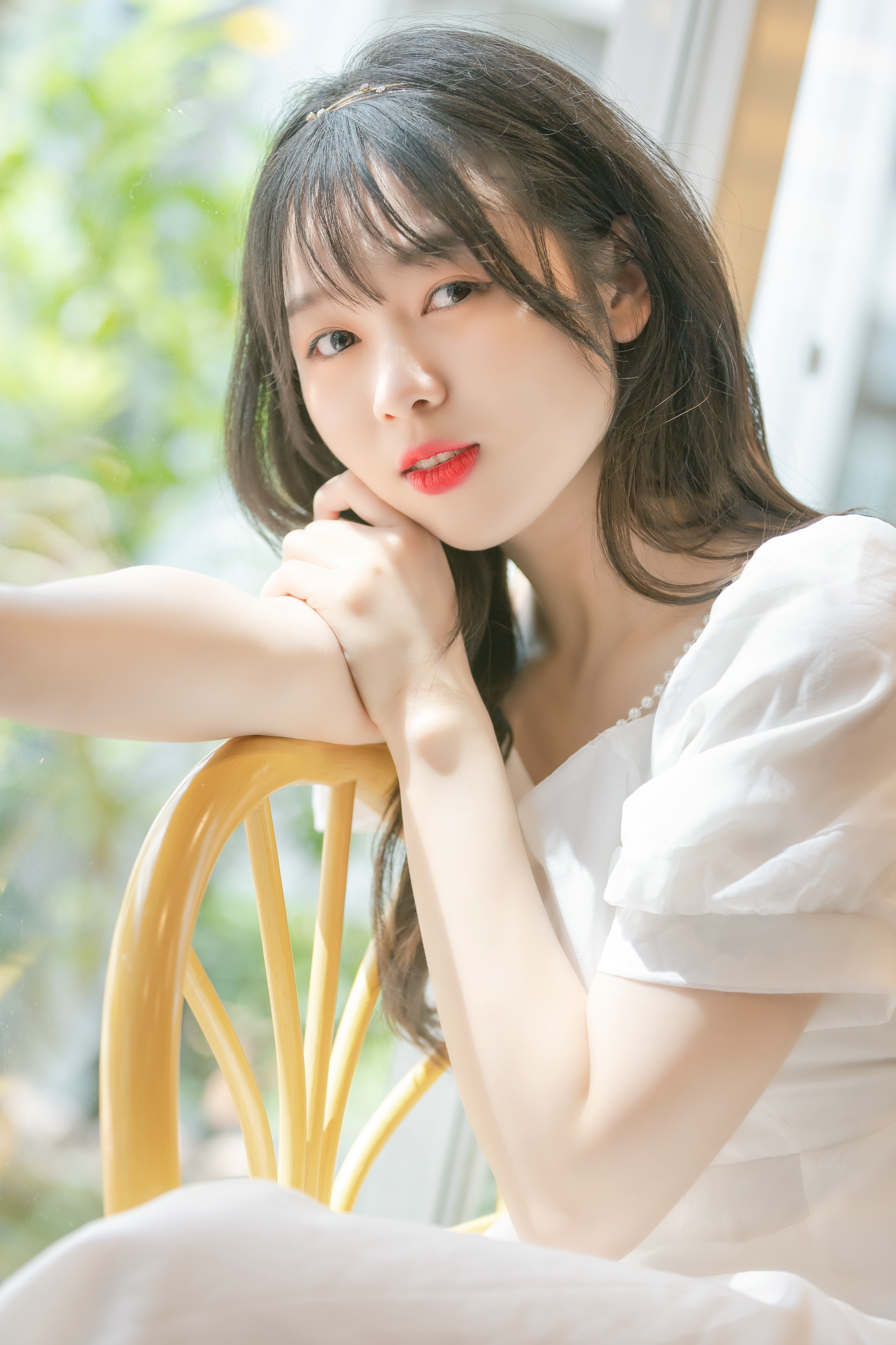 Close-up portrait of a young woman sitting on a chair in sunny indoor setting.