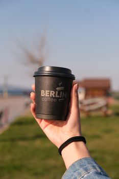 A hand holding a branded coffee cup with outdoor background and blurred scenery.