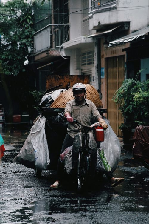 Free Man on tricycle with recycling bags in rainy urban street. Portrait shot. Stock Photo