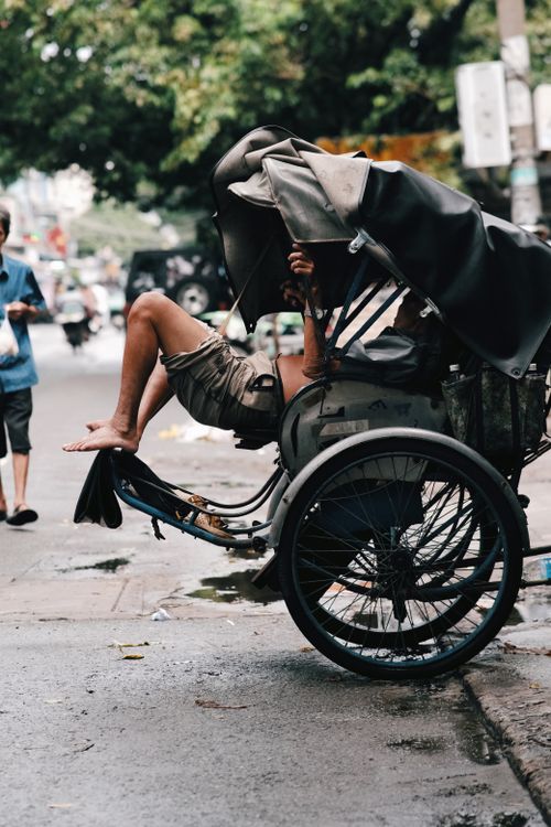 Free A person lying down and relaxing in a street rickshaw on a busy city street. Stock Photo