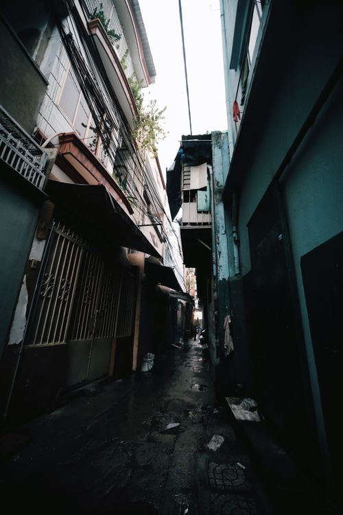 Free A narrow urban alley with tall buildings, capturing an empty and moody atmosphere. Stock Photo