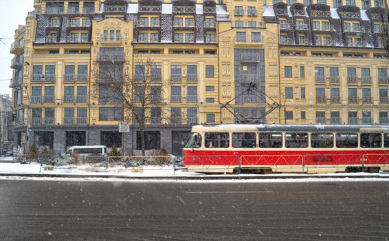 A vintage red tram travels through a snowy street in Kyiv with historic architecture in the background.