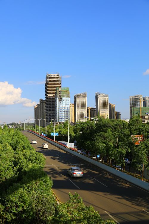 Free Vibrant urban cityscape featuring a skyline view, road traffic, and greenery under a blue sky. Stock Photo