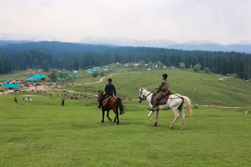 Free Two horseback riders traverse the lush, rolling hills of Yousmarg with stunning mountain views. Stock Photo
