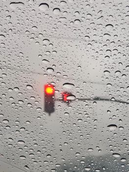 Blurred red traffic light seen through rain-covered window, creating a moody, atmospheric scene.