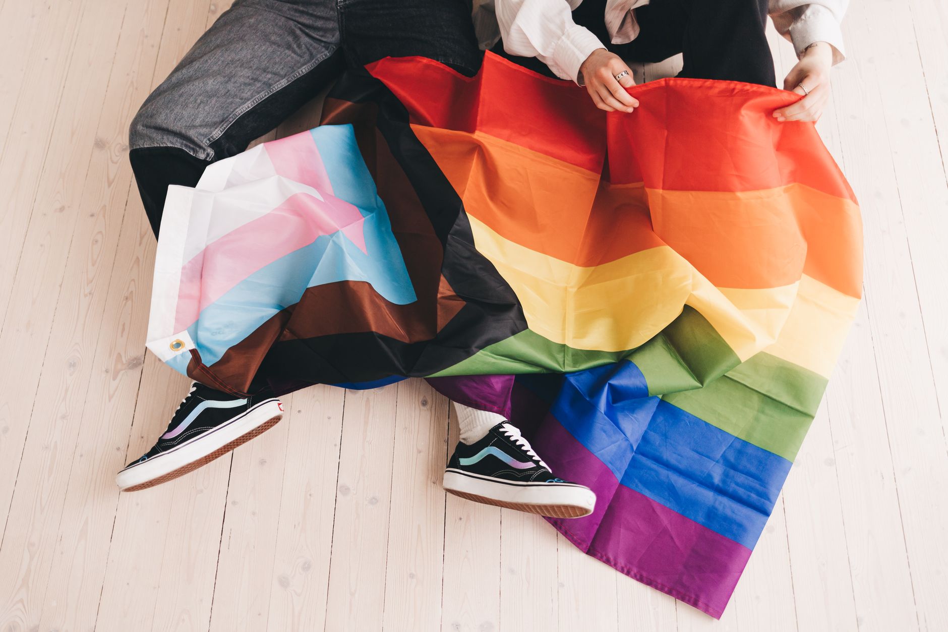 Two people sitting with Progress Pride flag, symbolizing LGBTQ+ inclusivity.