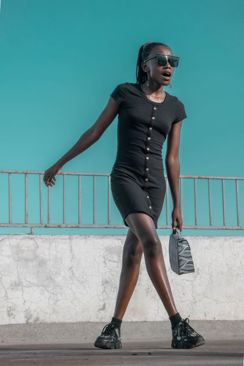 Free Stylish woman in black dress and sunglasses walking confidently under the sun. Stock Photo