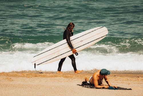 Free A Surfer Holding His Surfboard while Walking on a Beach Stock Photo
