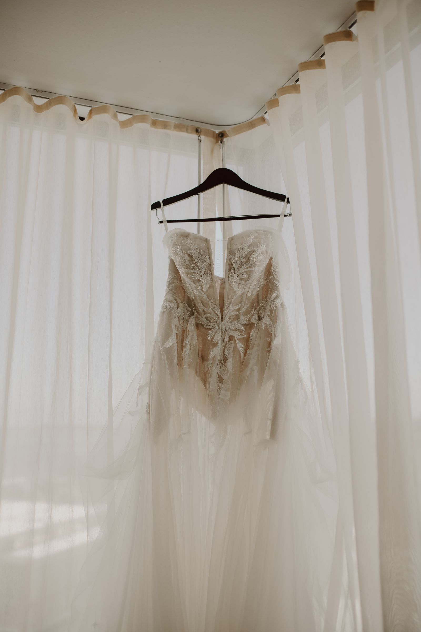 Intricate wedding gown hanging in soft natural light