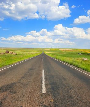 Straight highway through serene countryside with blue sky and clouds.