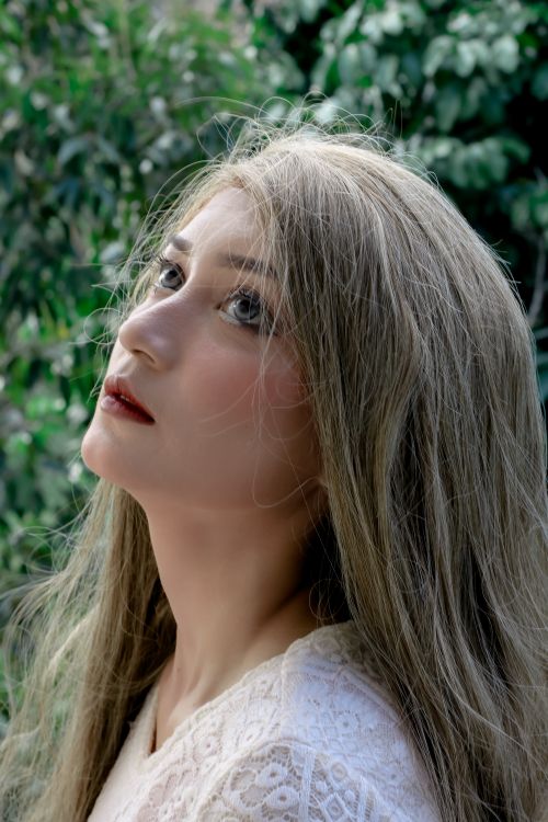 Free Close-up portrait of a young woman with blonde hair, looking up against a lush green background. Stock Photo