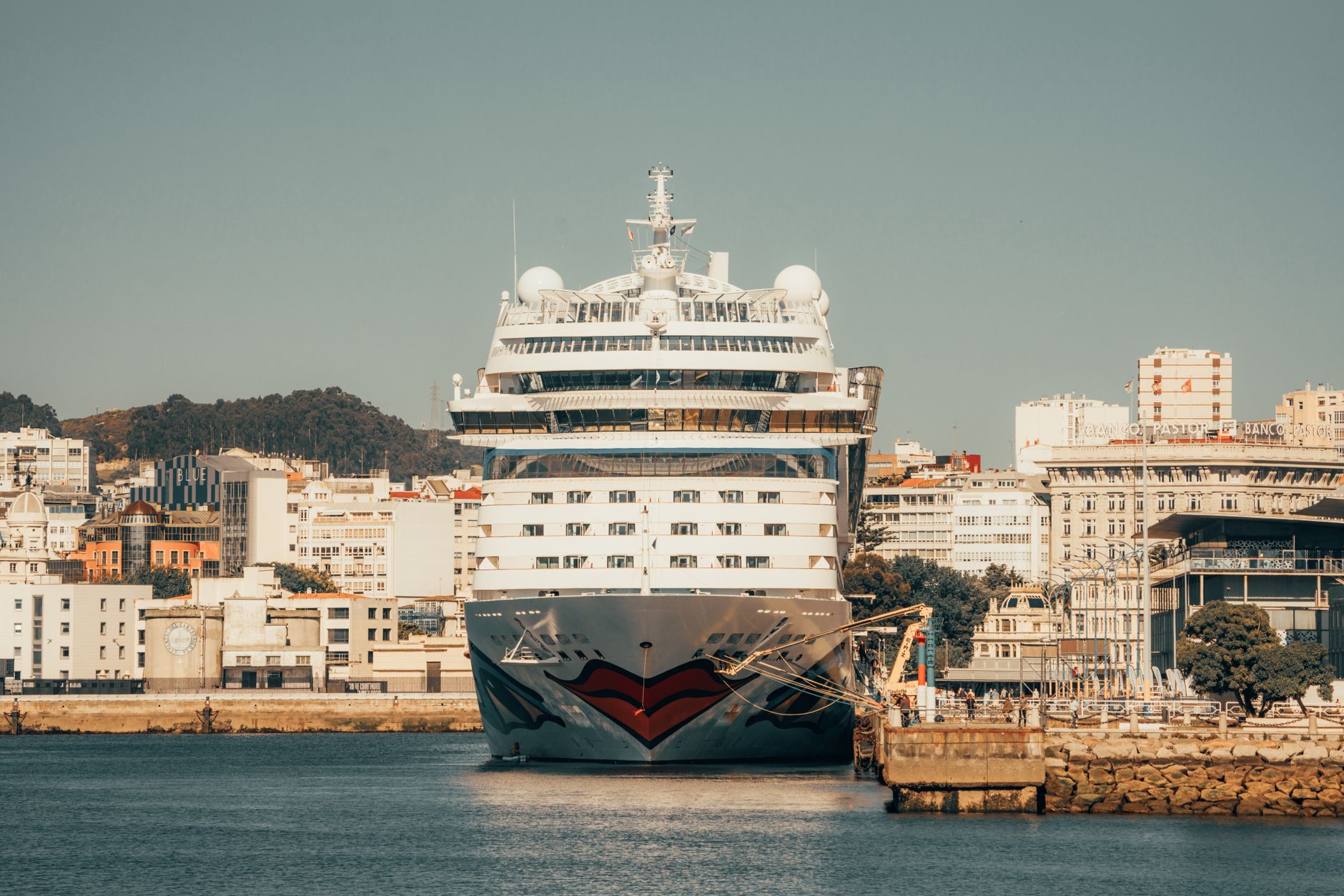 Massives Kreuzfahrtschiff, das in einem malerischen städtischen Hafen angedockt ist, mit lebendiger Architektur und klarem Himmel.