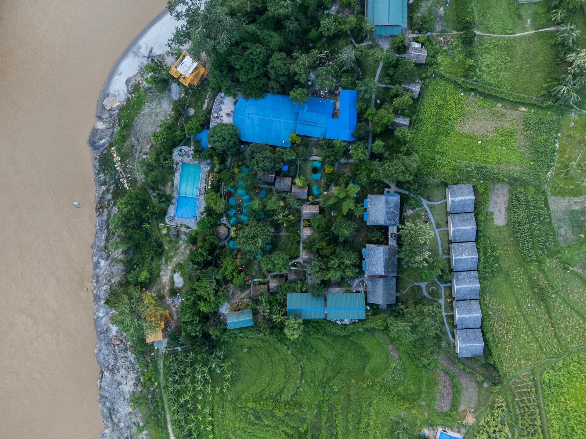 Aerial photography of a village with lush greenery, blue roofs, and a riverbank in Nepal.