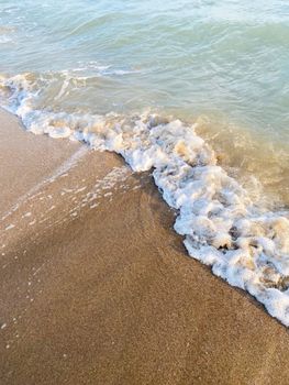 Close-up of sandy beach with gentle waves and sea foam, peaceful summer scene.