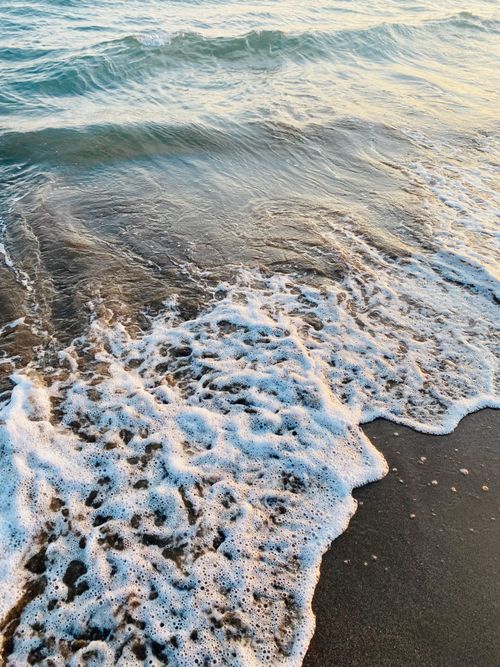 Free Gentle waves roll onto a sandy beach during dusk, creating a calming coastal scene. Stock Photo