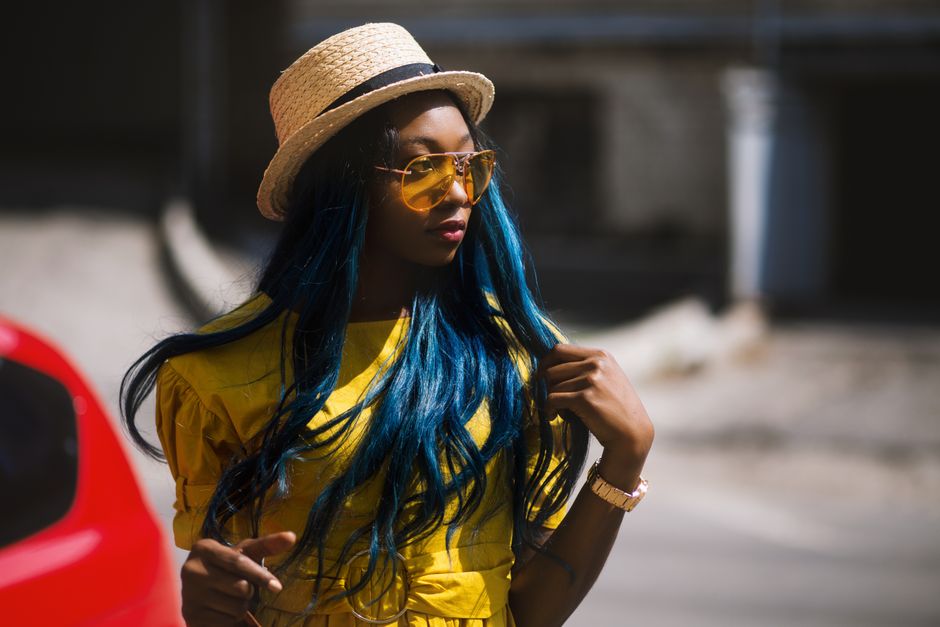 Fashionable woman in a yellow dress and sunglasses posing on a sunlit street.