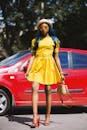 一位蓝发、身穿黄色连衣裙的时尚女子，在一辆红色汽车旁摆姿势