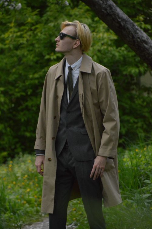 Free Man in sunglasses and trench coat against a lush green backdrop. Stock Photo