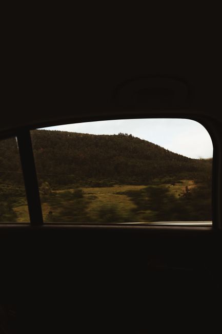 A tranquil view of rolling hills captured through a car window on a sunny day, conveying a sense of travel and adventure.