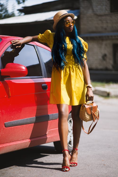 Mujer En Mini Vestido Amarillo Sosteniendo Bolso Al Lado De Coche Rojo