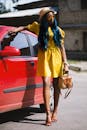 阳光明媚的日子里，一位穿着黄色连衣裙和红色高跟鞋的时尚女人在车旁摆着姿势