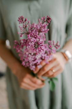 A delicate close-up of a woman holding a bouquet of pink lilac flowers in gentle focus.