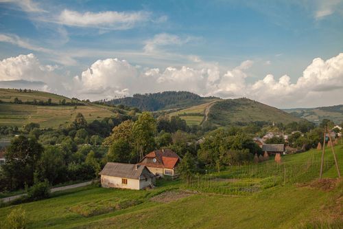 Free Picturesque view of rural Ukraine with rolling hills, a house, and vibrant greenery under a cloudy sky. Stock Photo