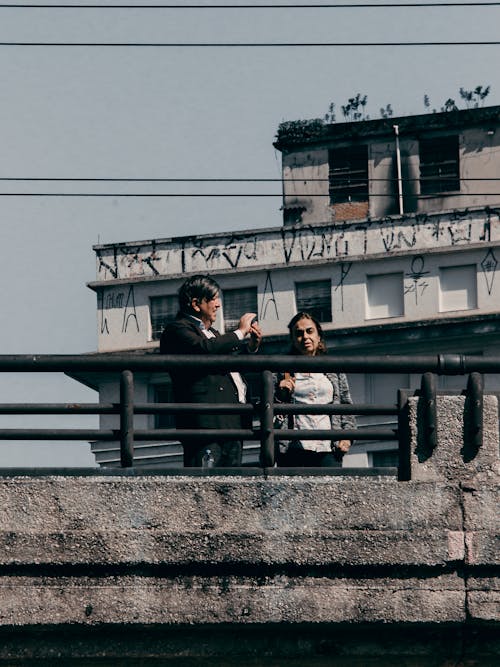 A Man and a Woman Standing on a Bridge Near Old Concrete Building