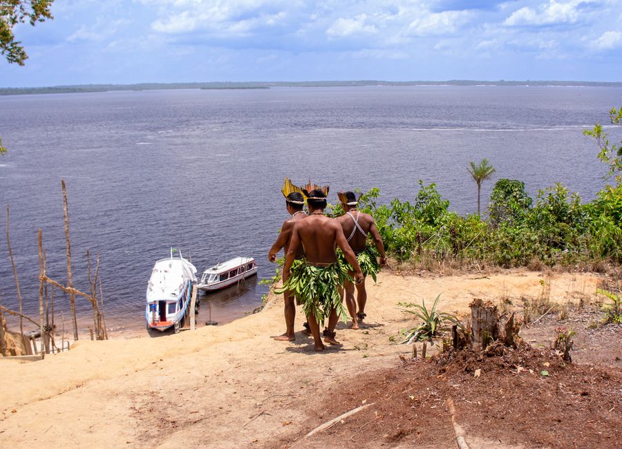 Indigenous men in traditional attire overlooking boats on the Amazon River.