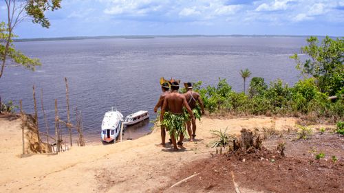 Free Indigenous men in traditional attire overlooking boats on the Amazon River. Stock Photo