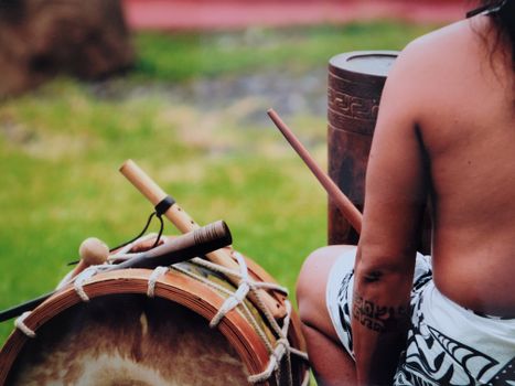 A person with cultural tattoos plays traditional drums outdoors, showcasing cultural heritage.