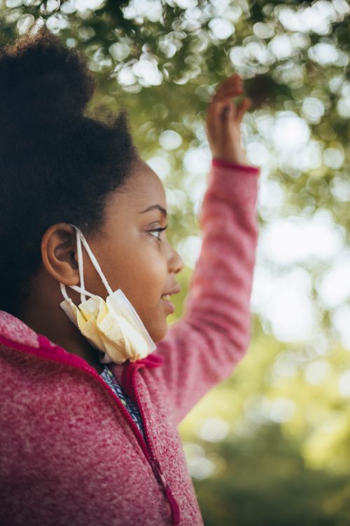 Free Profile of a young girl with afro hair wearing a red hoodie, lowering her face mask outdoors. Stock Photo