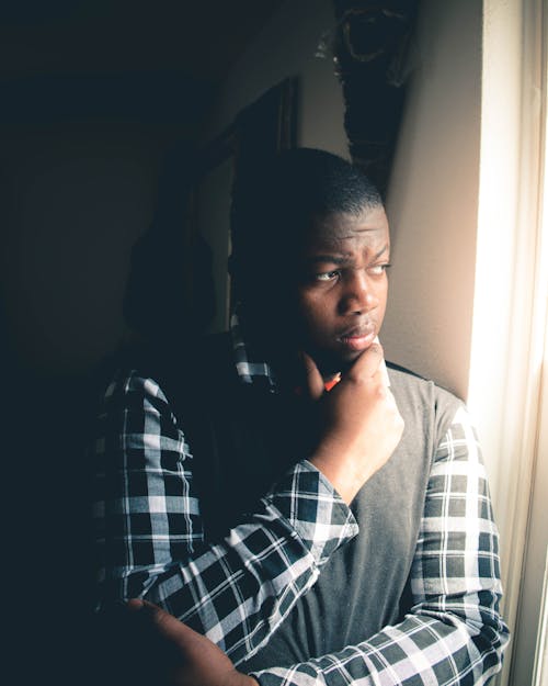 A Man Wearing Plaid Long Sleeves Standing Beside the Window while Looking Afar