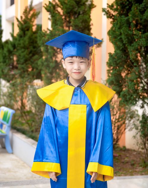 Free Smiling child in blue and yellow graduation gown outdoors, celebrating achievement. Stock Photo