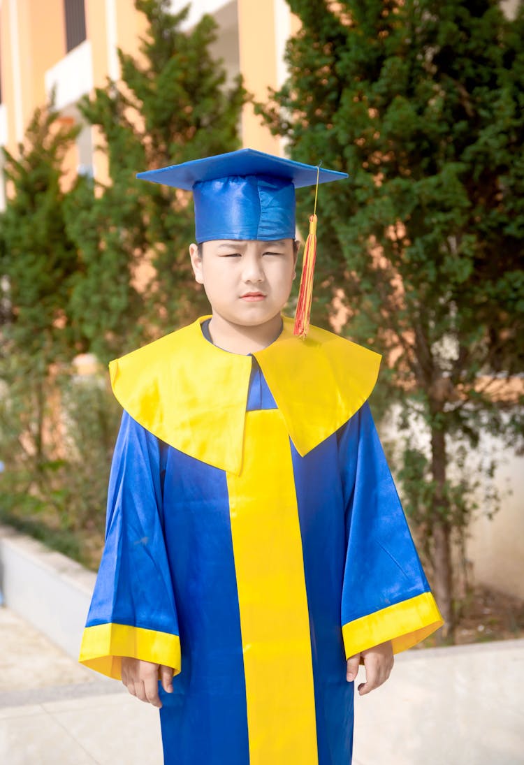 A Grumpy Boy Wearing Blue Academic Dress Looking At The Camera