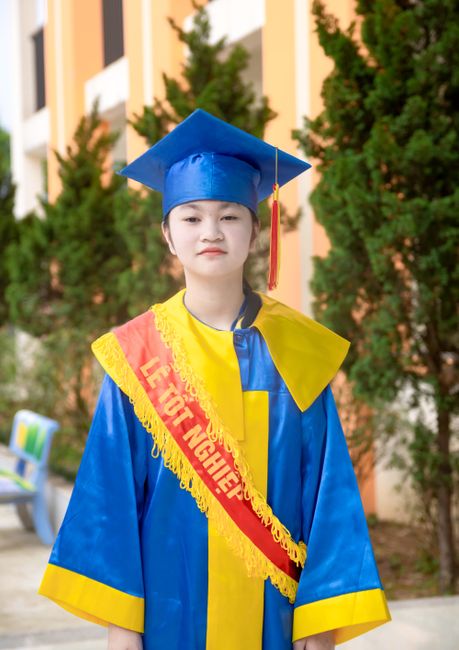 Nên Ăn Hạt Macca Lúc Nào Trong Ngày Để Hấp Thu Trọn Vẹn Dinh Dưỡng? 5 Portrait of a young woman in graduation attire, standing outdoors with trees in the background.