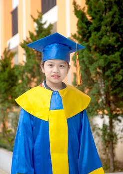 Young girl smiling in blue and yellow graduation attire, outdoors, celebrating success.