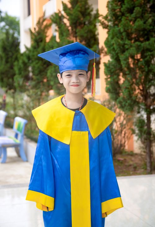 Free Smiling child in blue and yellow graduation gown with cap standing outdoors. Stock Photo