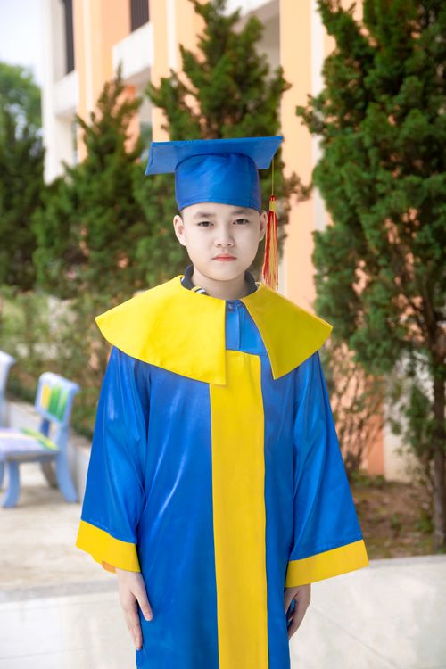 Free A young graduate wearing a blue and yellow cap and gown, posing outdoors with a calm expression. Stock Photo